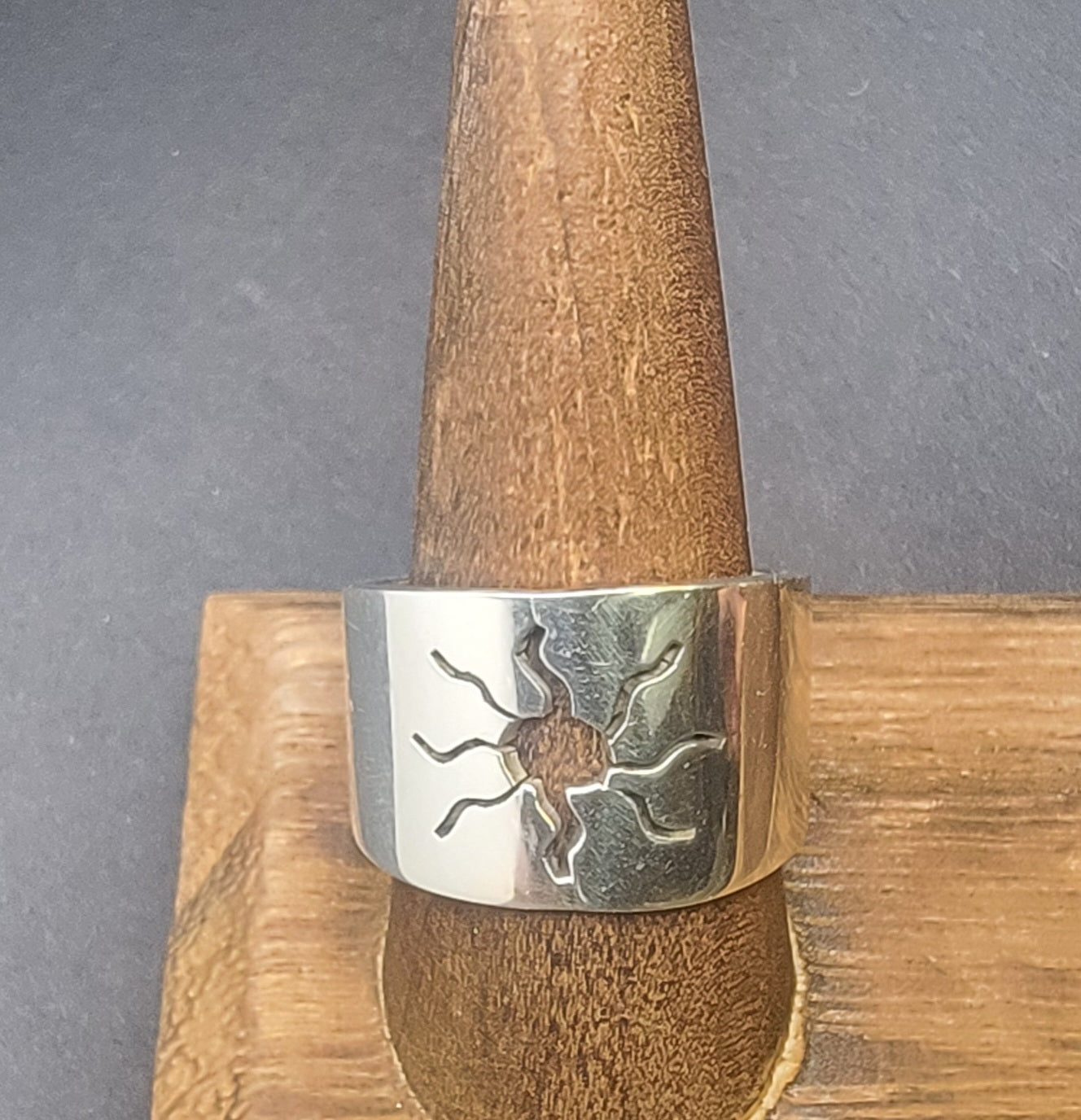 The 925 Sterling Silver Wideband Sunburst Ring elegantly showcased on a wooden stand, emphasizing its modern artisan craftsmanship. This statement ring, with its sun cutout design, is the perfect blend of casual jewelry and celestial inspiration, making it an essential piece for summer wardrobes.