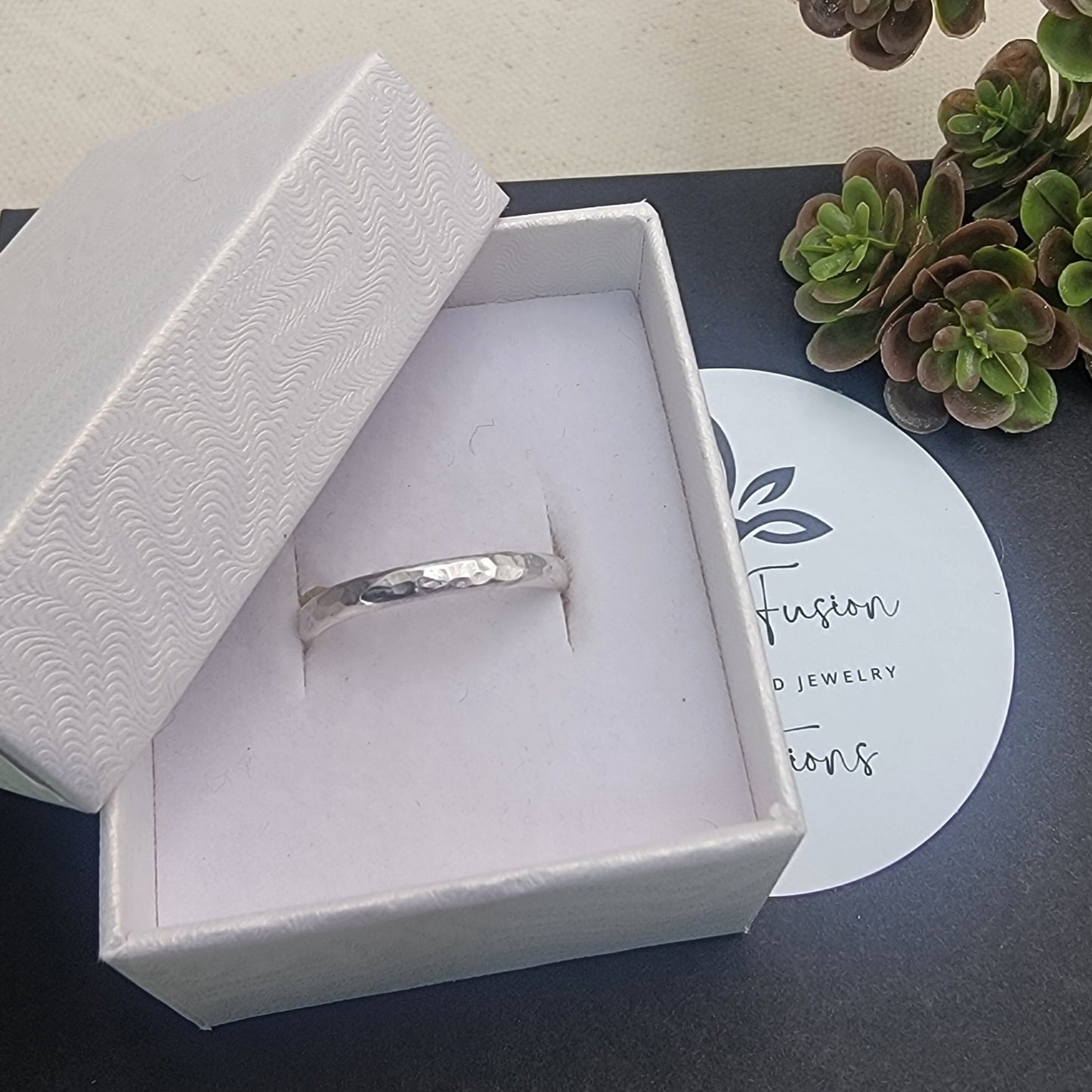 Silver ring in a white box with a plant in the background