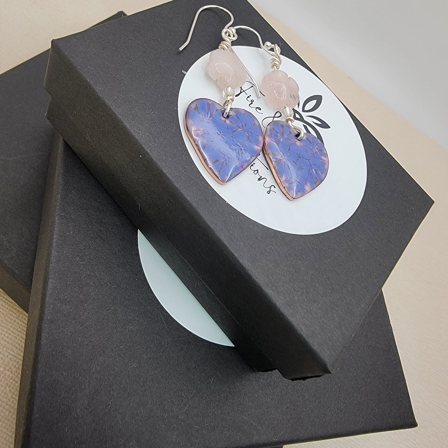 Heart-shaped earrings with pink and purple stones on a black jewelry box