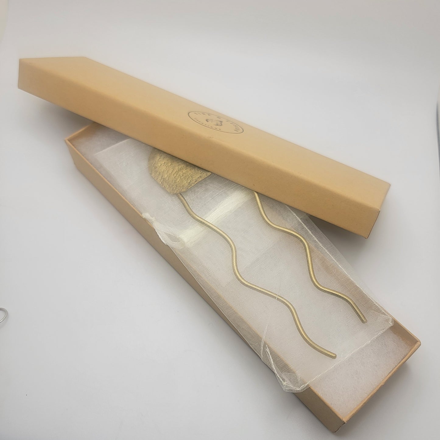 Brass hair pin in a beige box on a white background