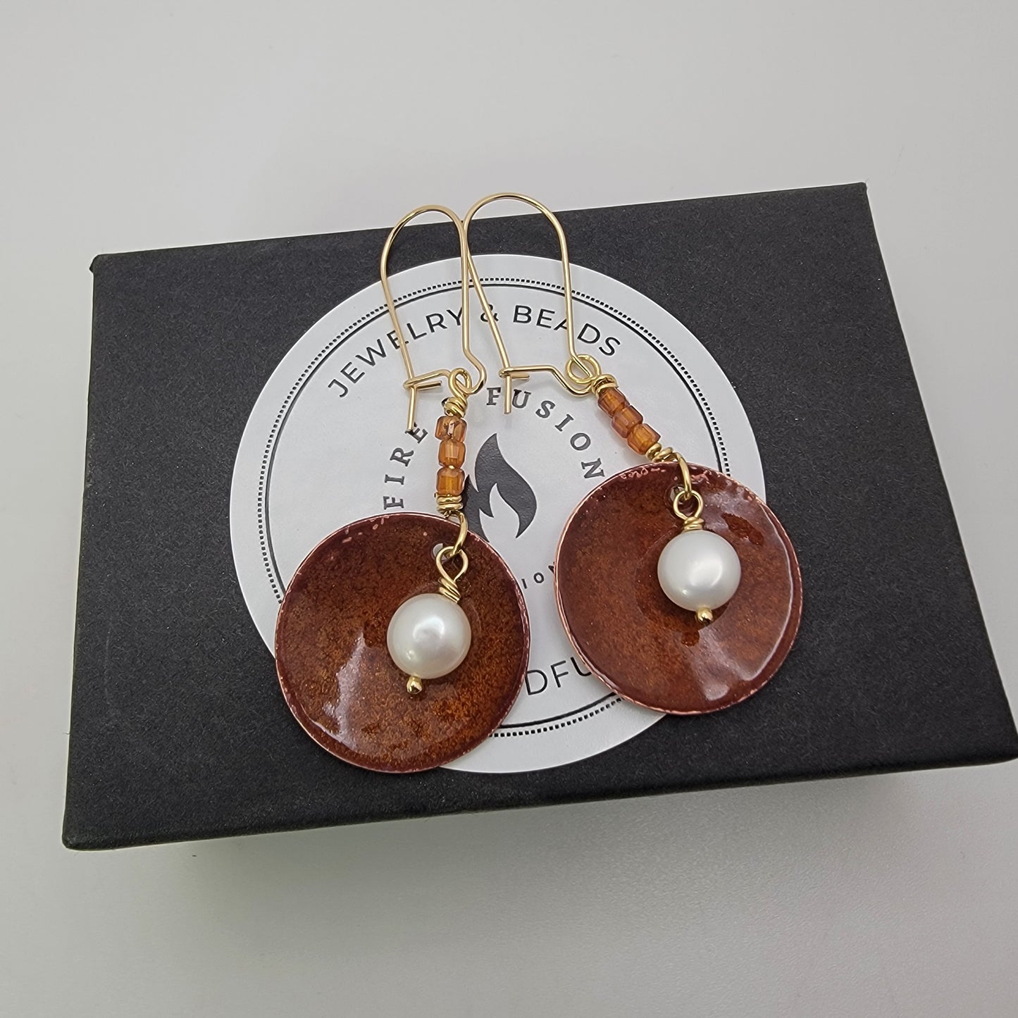 Brown circular earrings with pearl-like beads on a jewelry box
