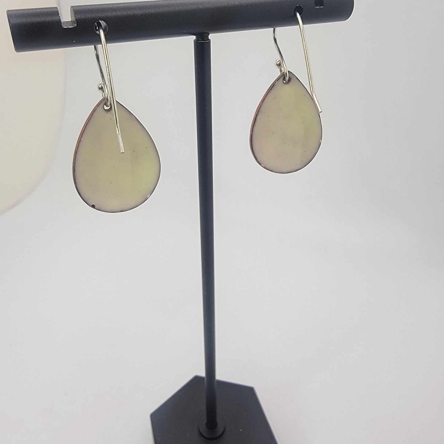 A pair of yellow earrings on a black earring stand on a white background