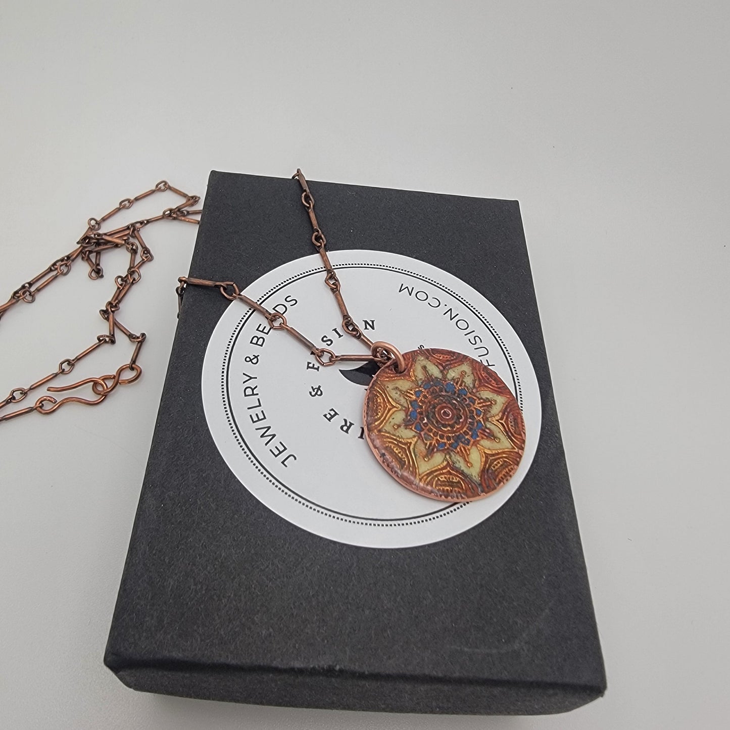 Necklace with a decorative mandala pendant on a branded card against a gray background