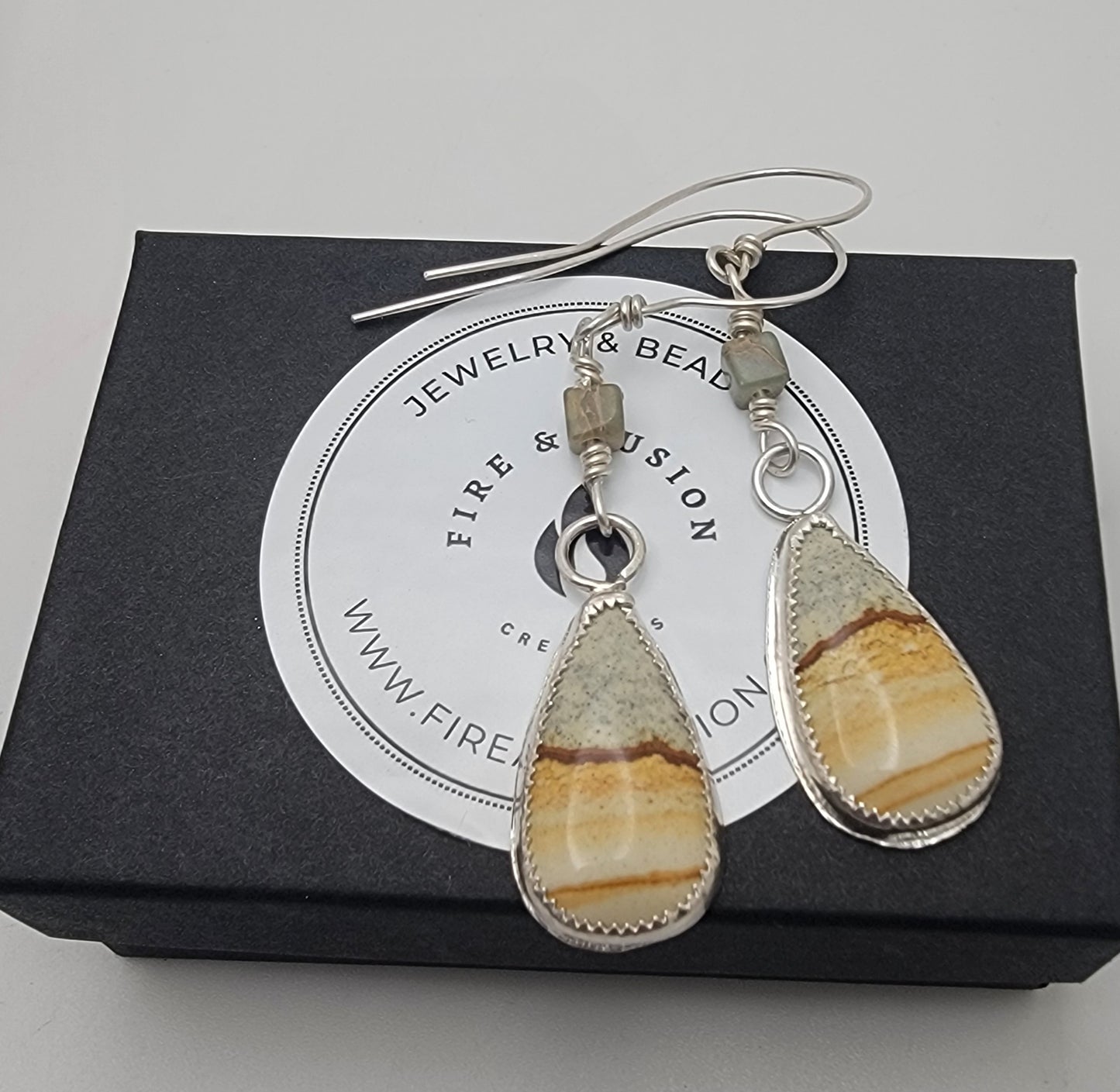 Petrified wood and sterling silver teardrop shaped dangle earrings being shown on black branded gift box