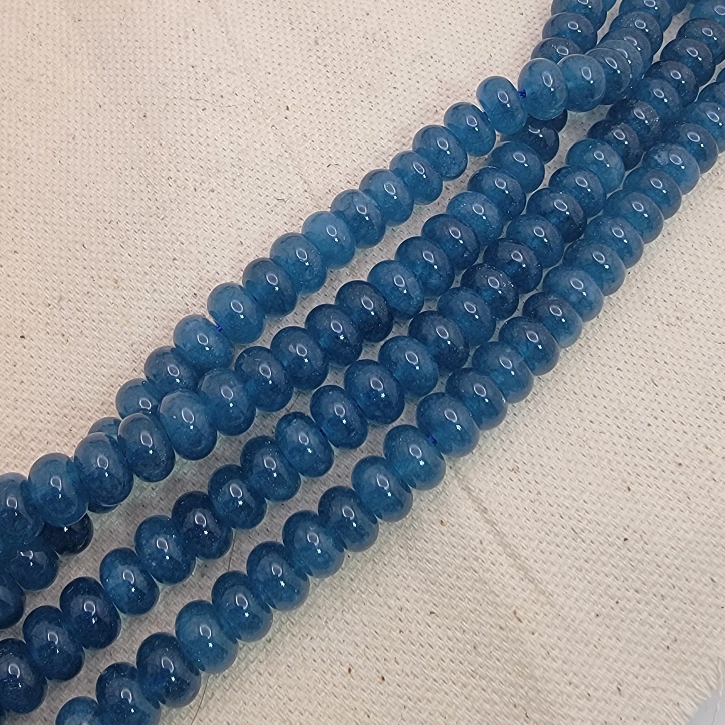 Two strands of blue kyanite gemstone beads on a textured beige surface