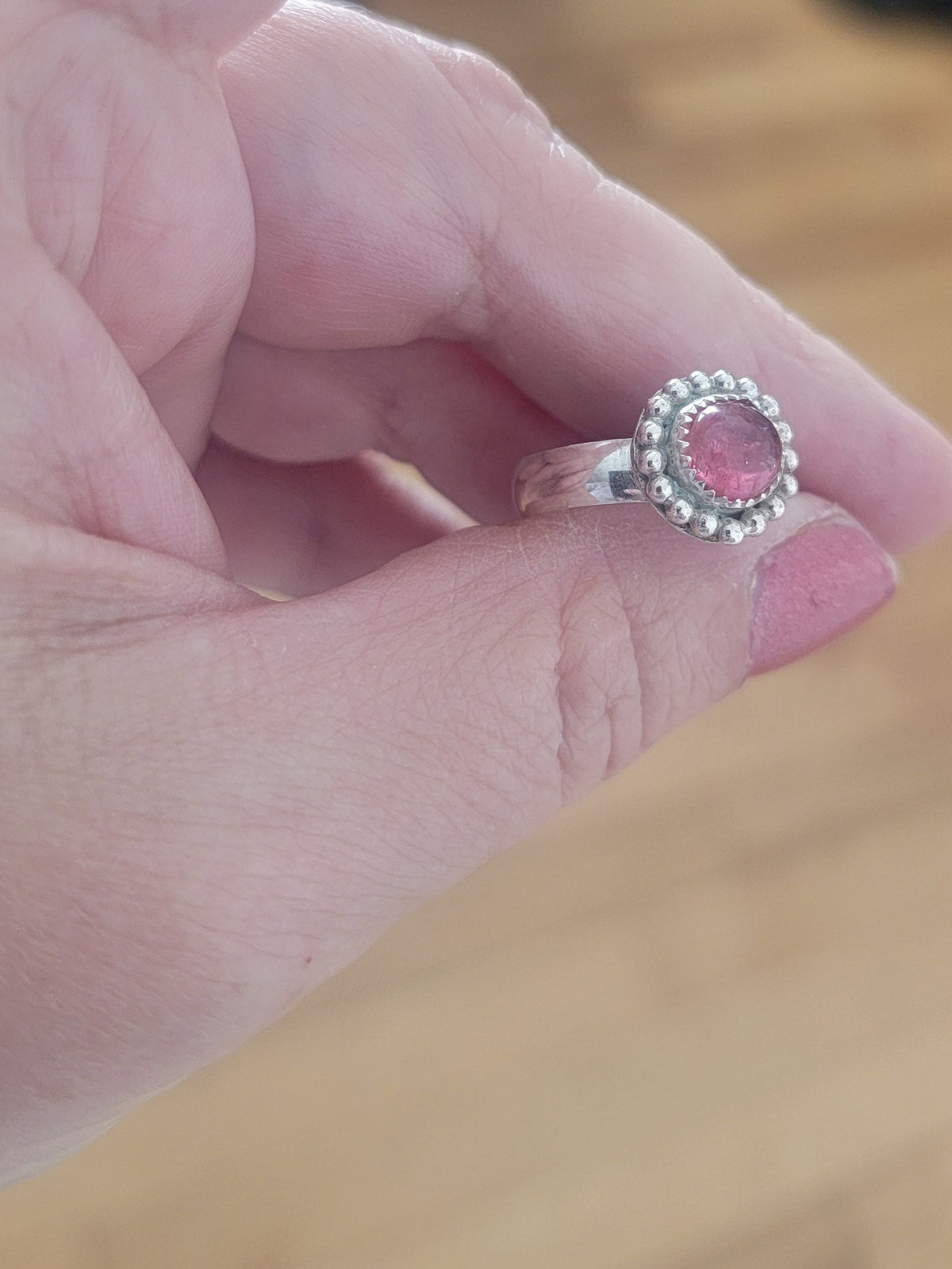Pink Tourmaline and Sterling silver ring with bead detail around the bezel being held in a hand