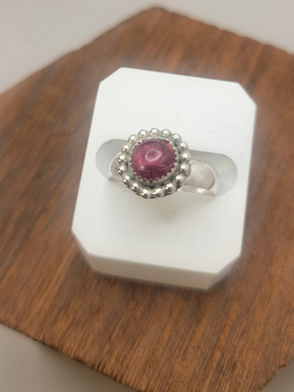Pink Tourmaline and Sterling silver ring with bead detail around the bezel in white ring display on wood platform 