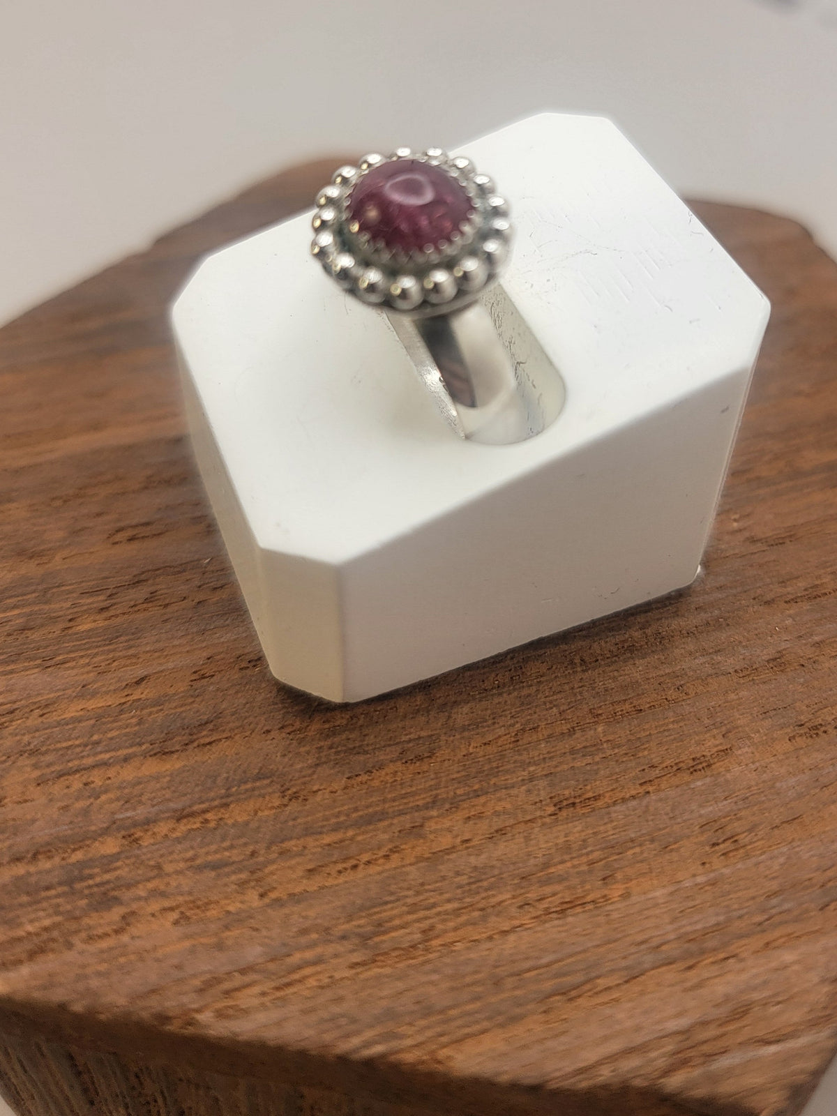 Side view of a Pink Tourmaline and Sterling silver ring with bead detail around the bezel in white ring display on wood platform 