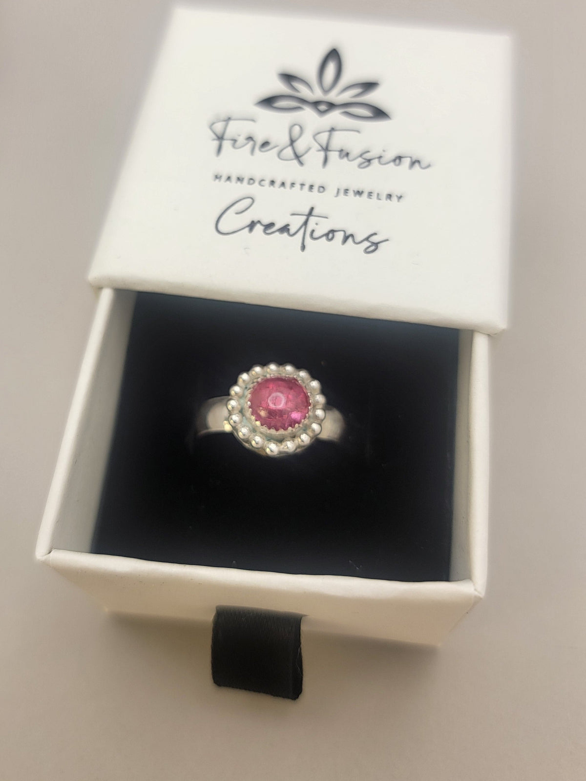 Pink Tourmaline and Sterling silver ring with bead detail around the bezel in white branded gift box that has the text 'Fire and Fusion Creations Handcrafted Jewelry'