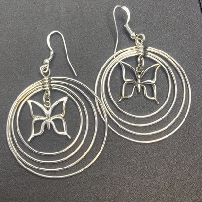 Sterling silver concentric hoop earrings (2¼″ × 1½″) featuring four graduated rings framing a delicate butterfly charm.