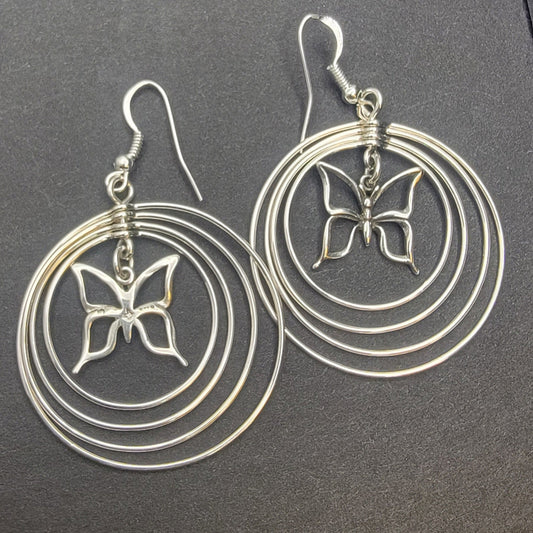 Sterling silver concentric hoop earrings (2¼″ × 1½″) featuring four graduated rings framing a delicate butterfly charm.
