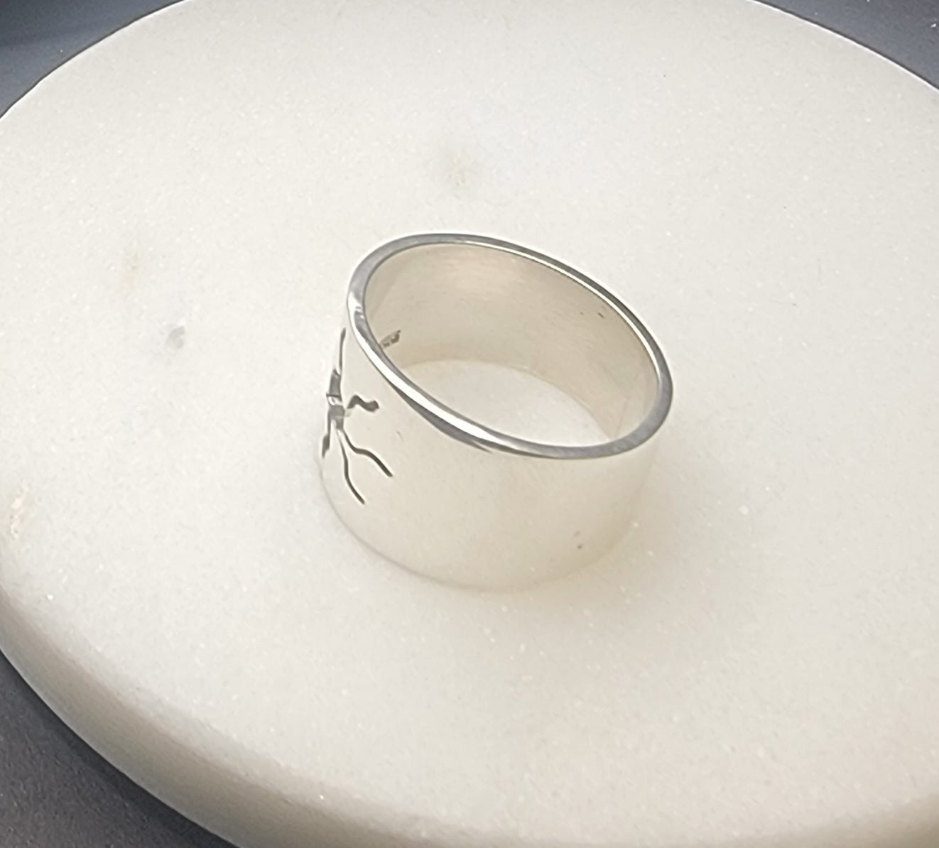 Artistic display of the 925 Sterling Silver Wideband Sunburst Ring on a soft surface, showcasing its distinctive sunburst pattern. This bold artisan ring is an everyday statement piece that enhances any outfit with its radiant and sun inspired jewelry design.