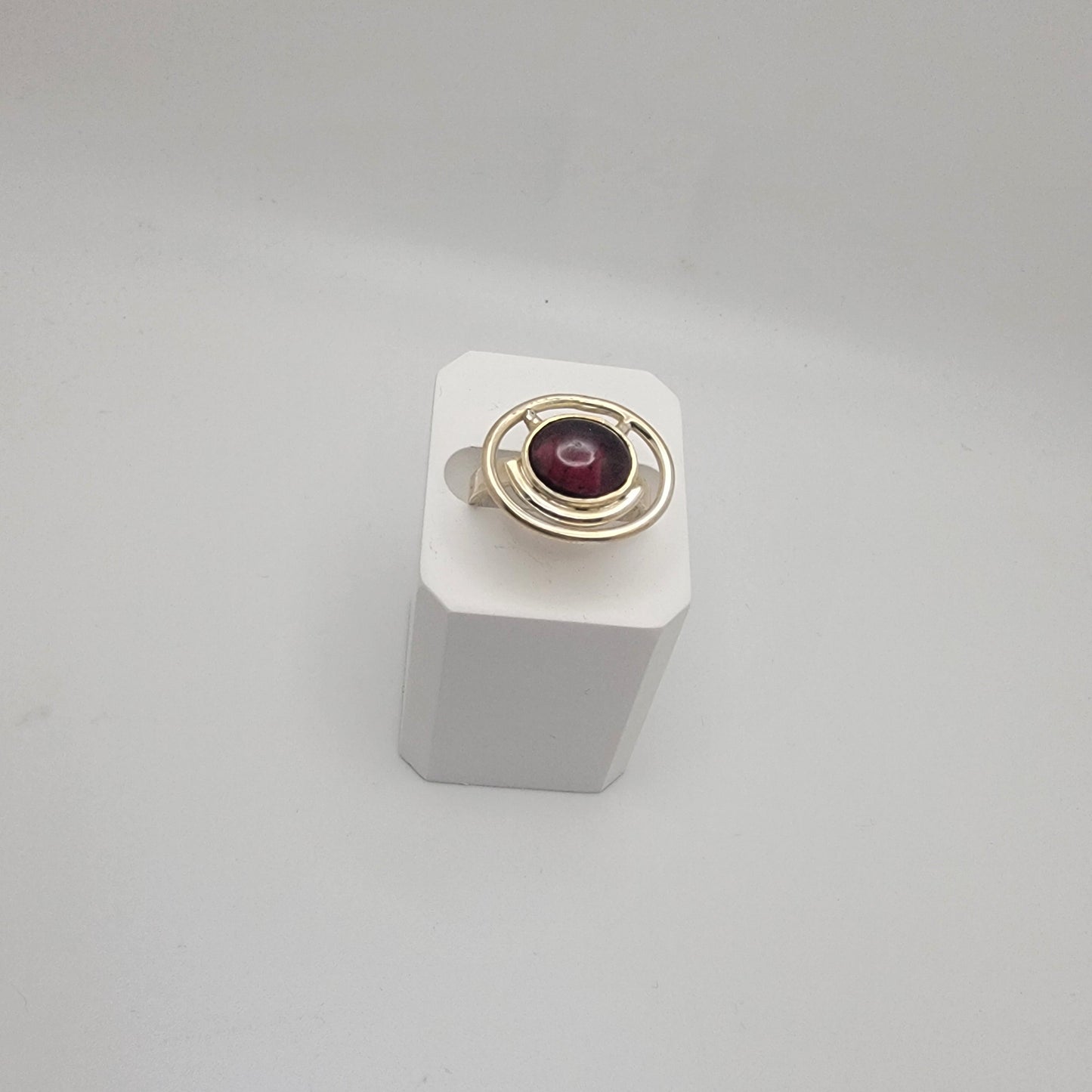 Sterling silver ring with a 12×10 mm oval garnet cabochon set on a uniform 3 mm band, displayed on a white stand.