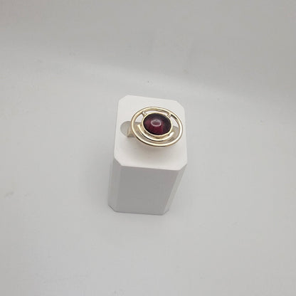 Sterling silver ring with a 12×10 mm oval garnet cabochon set on a uniform 3 mm band, displayed on a white stand.