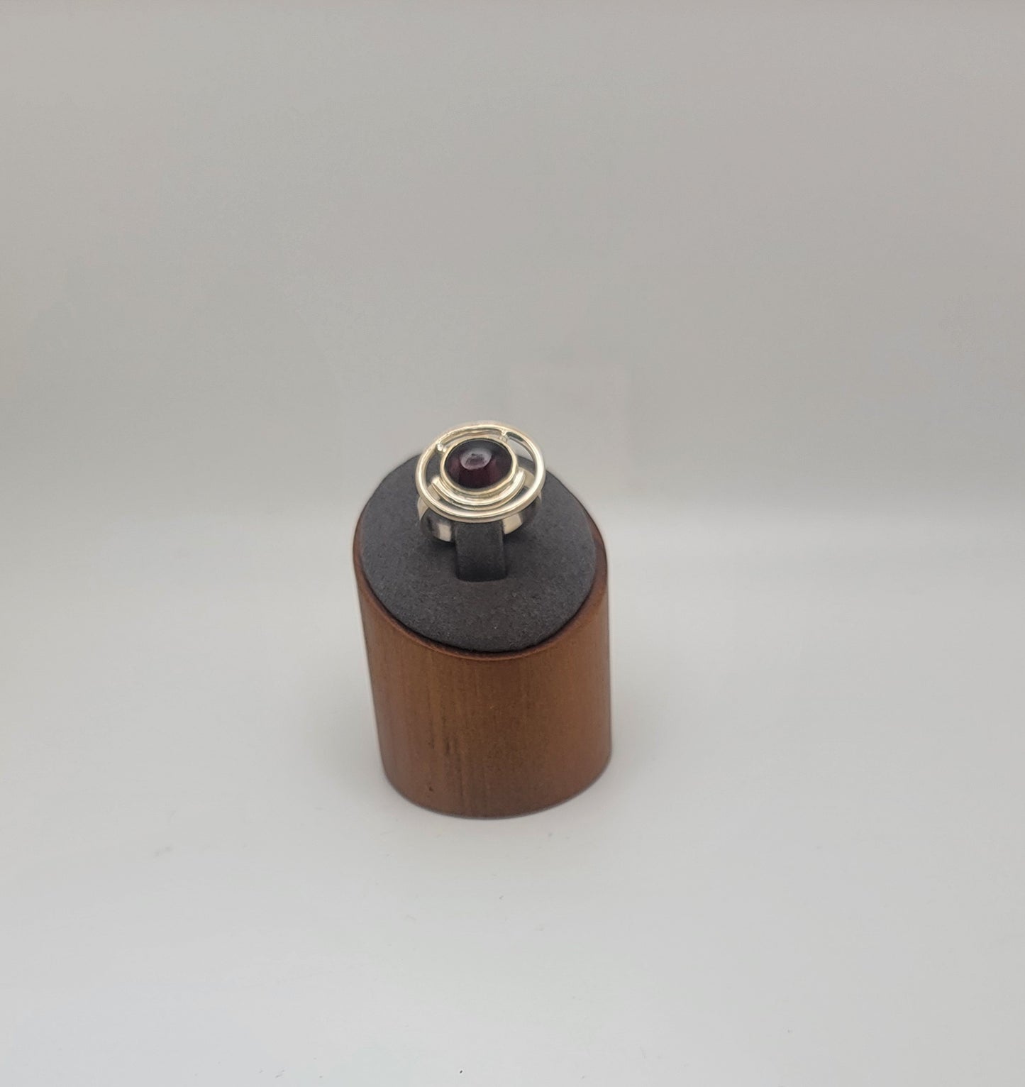 Sterling silver ring with a 12×10 mm oval garnet cabochon set on a uniform 3 mm band, displayed on a wooden stand.