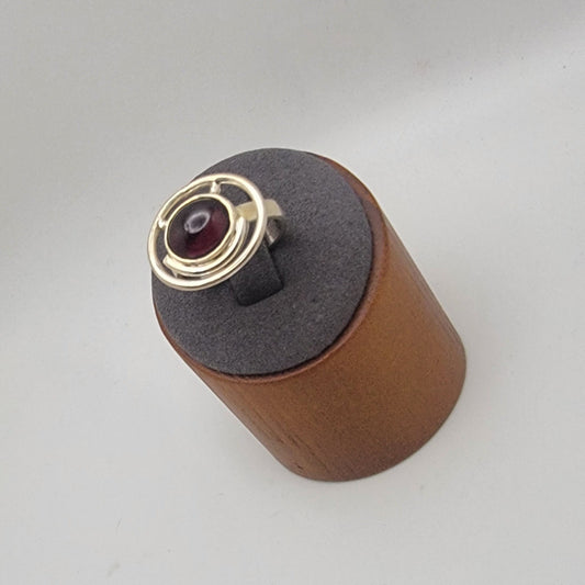 Sterling silver ring with a 12×10 mm oval garnet cabochon set on a uniform 3 mm band, displayed on a wooden stand.