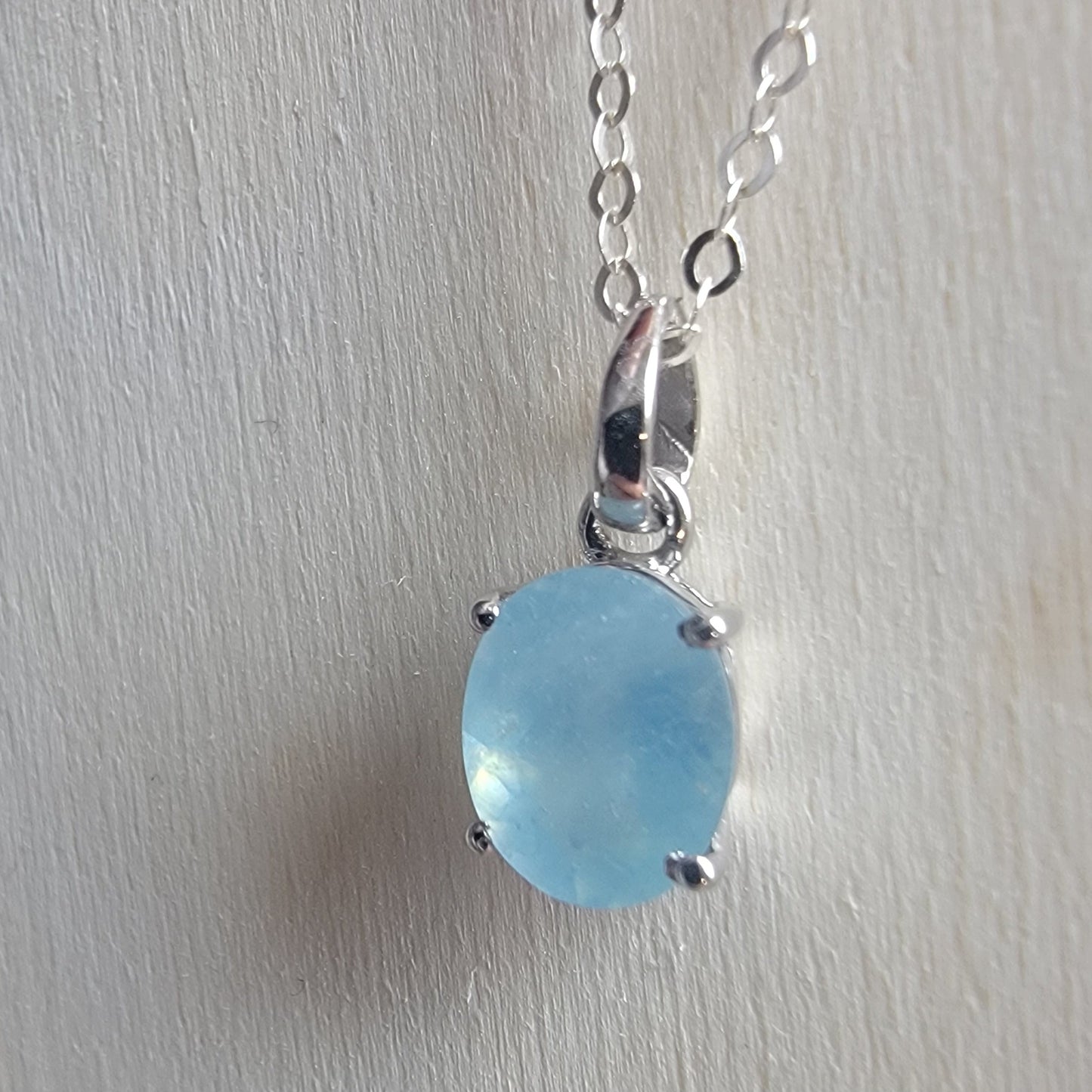 Silver necklace with a blue pendant on a light gray background