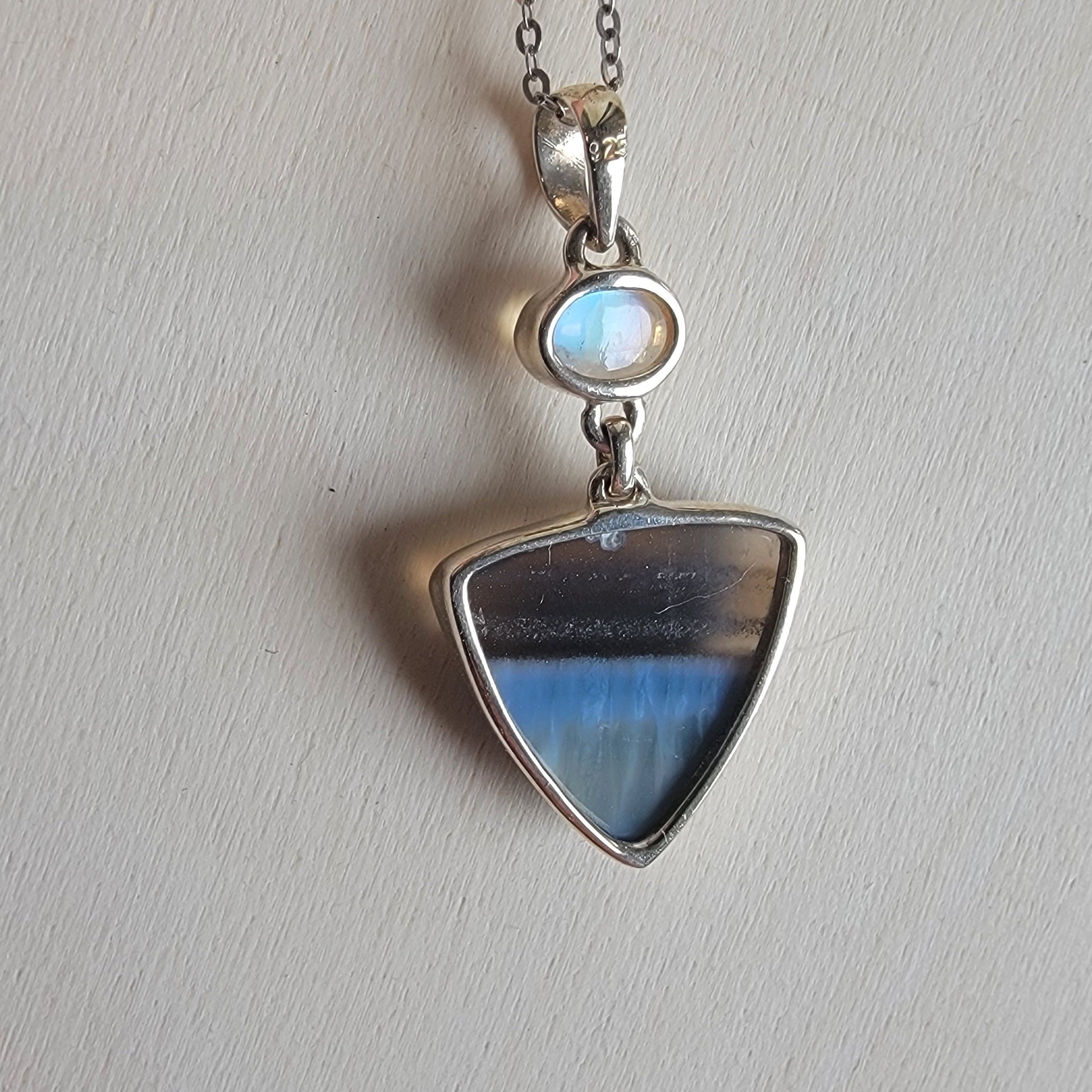 Silver pendant with a blue stone on a light gray background