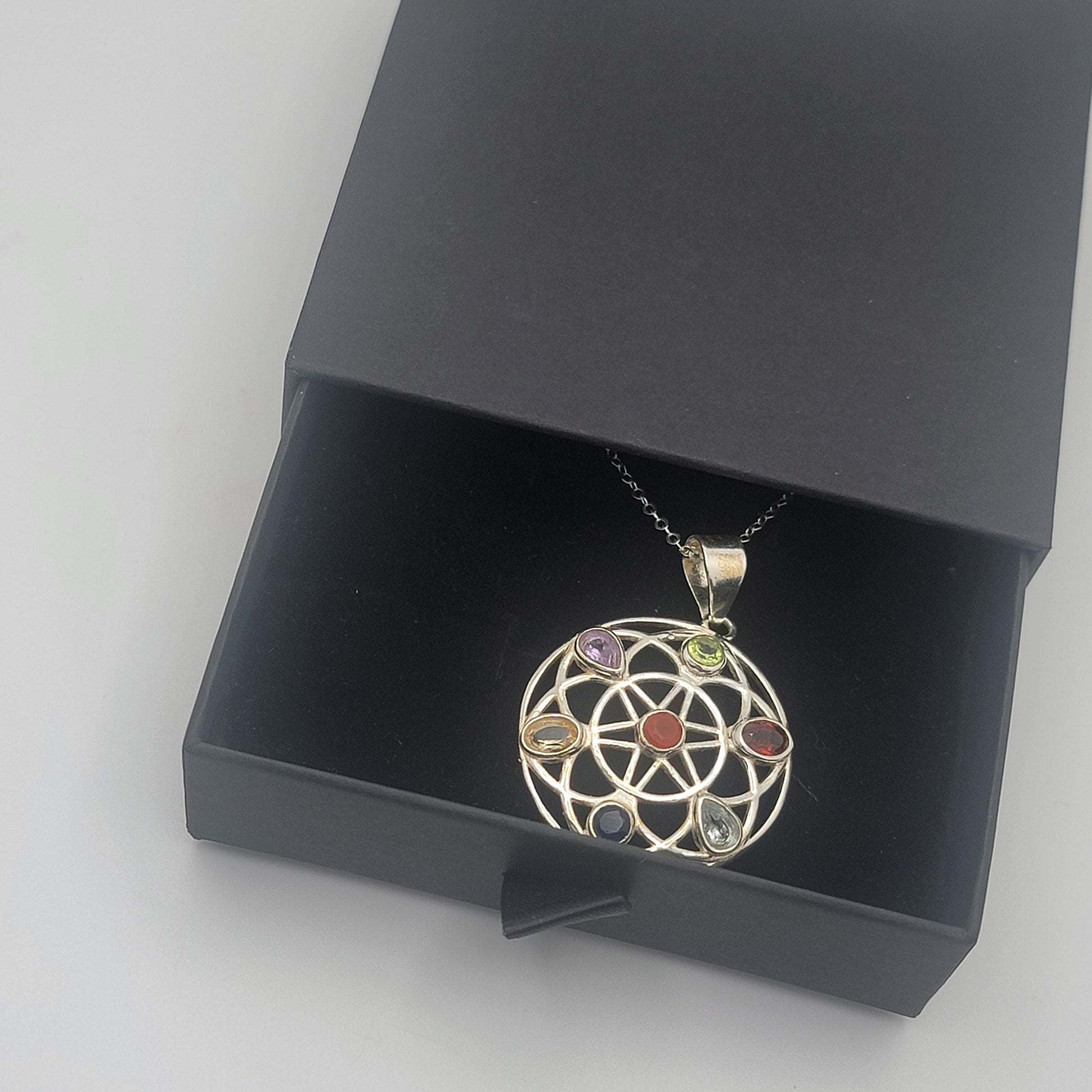 Jewelry pendant with colored stones in a black box on a light gray background