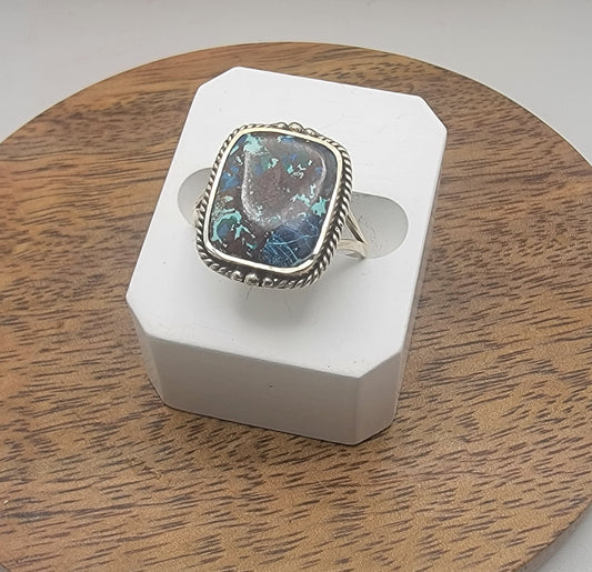 Ring with a colorful stone on a white stand against a wooden background
