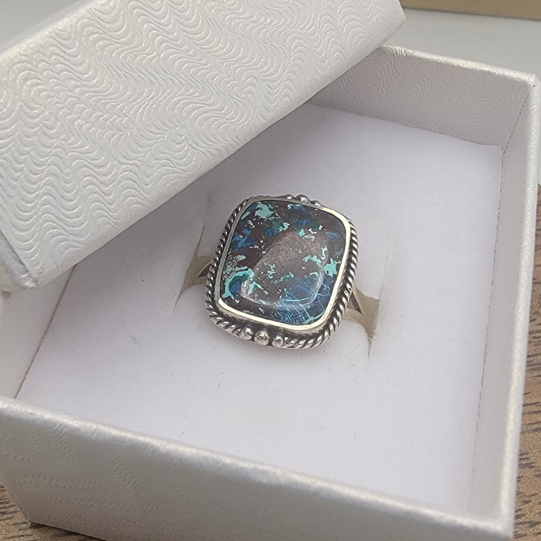 Silver ring with a colorful stone in a white box