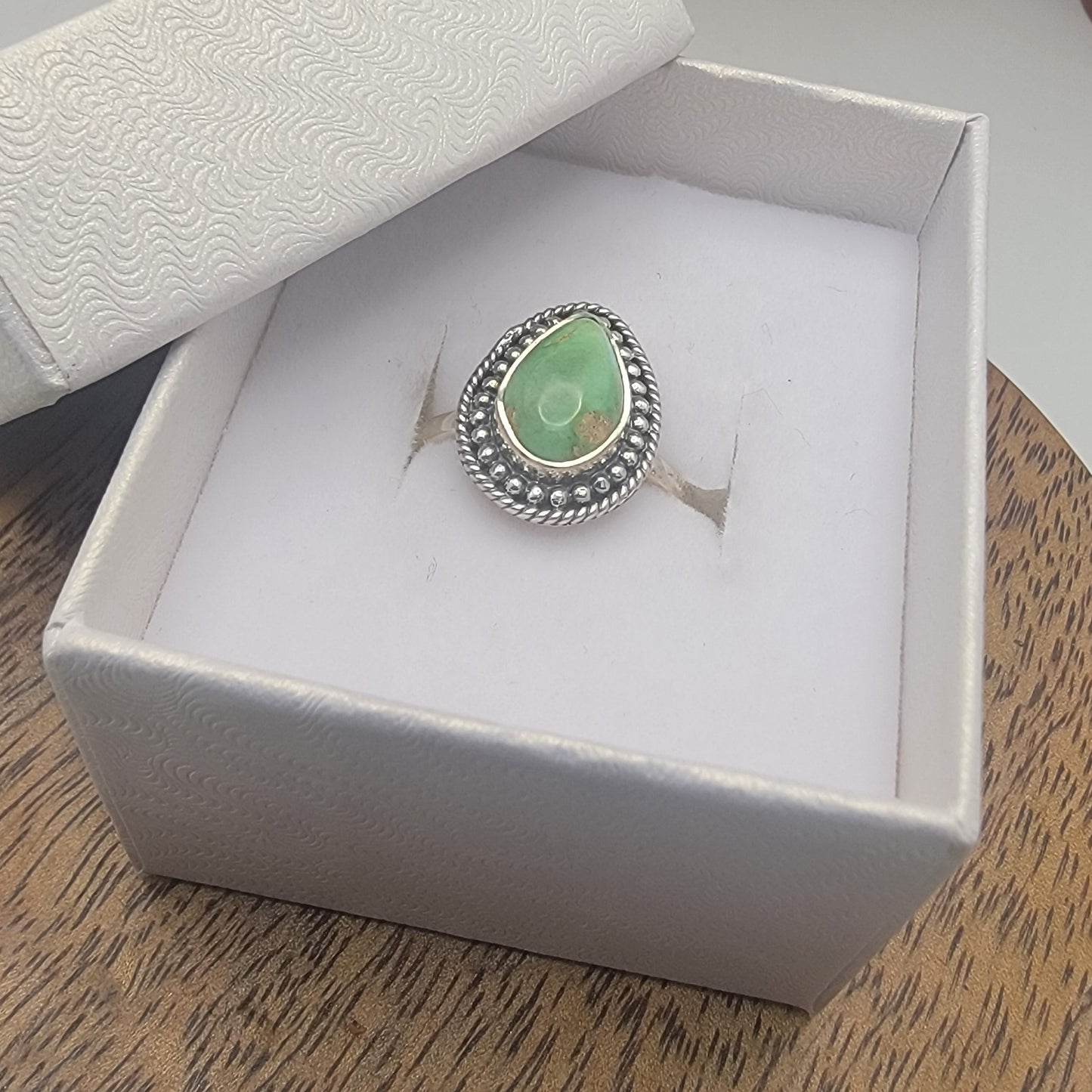 Ring with a green gemstone in a white box on a wooden surface