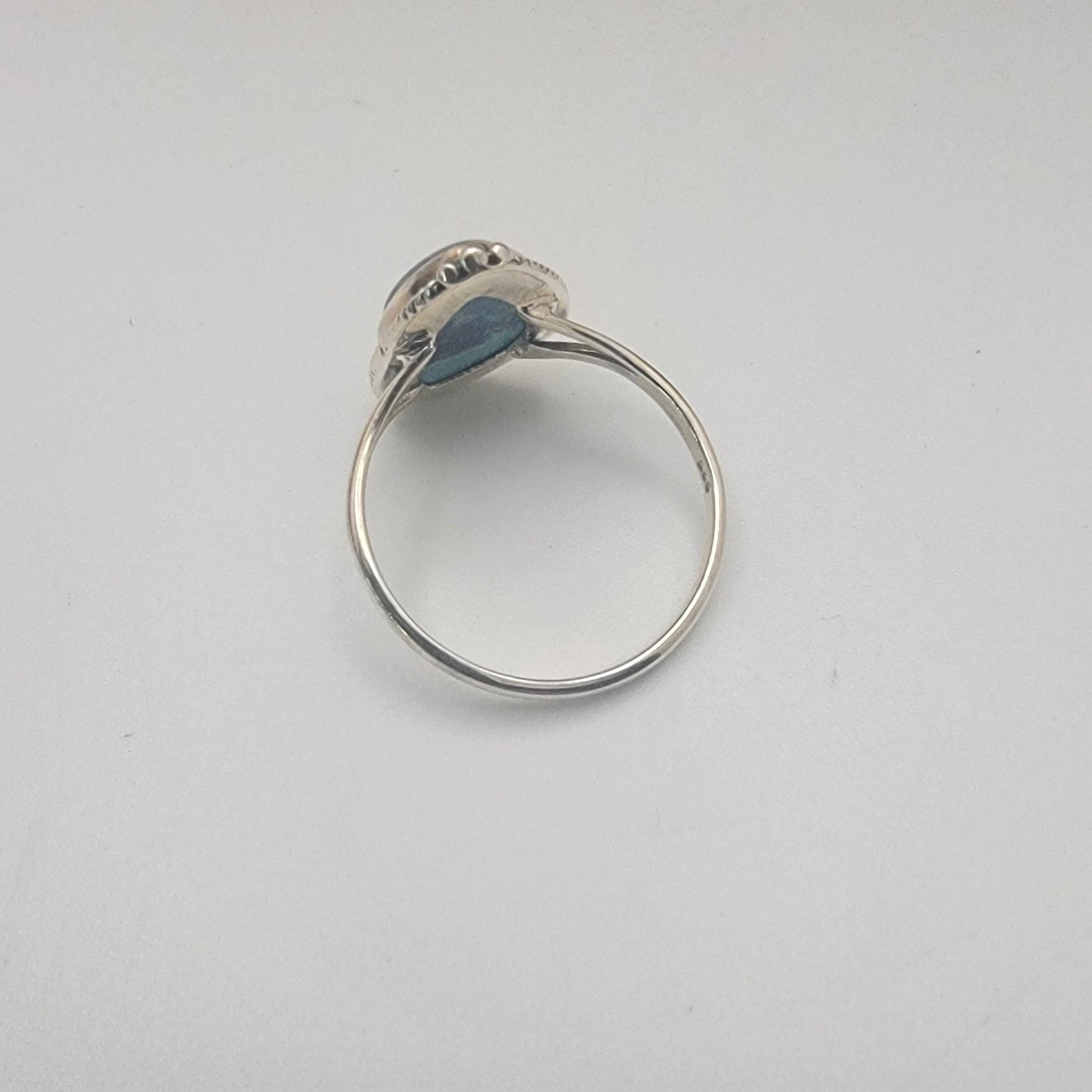 Silver ring with blue stone on a white surface next to a ruler for size reference.
