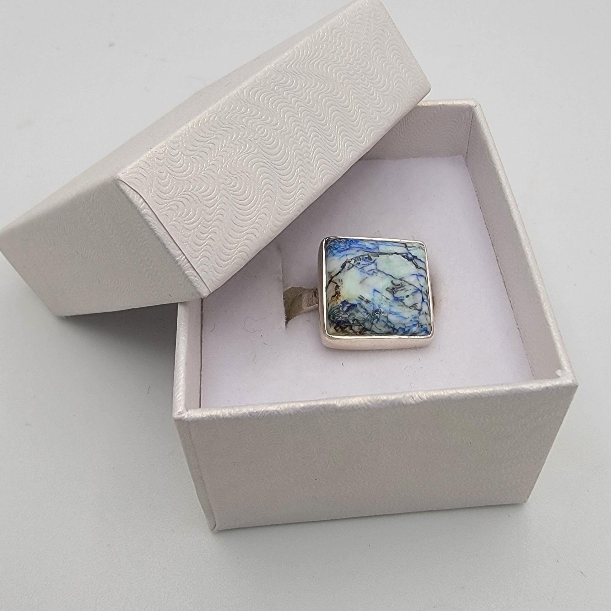 Square ring with blue and green pattern in a white box on a light gray background