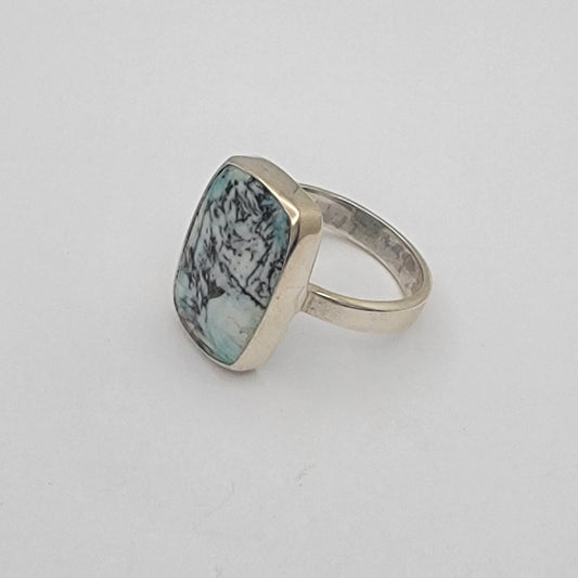 Silver ring with a green, black and white gemstone on a light gray background
