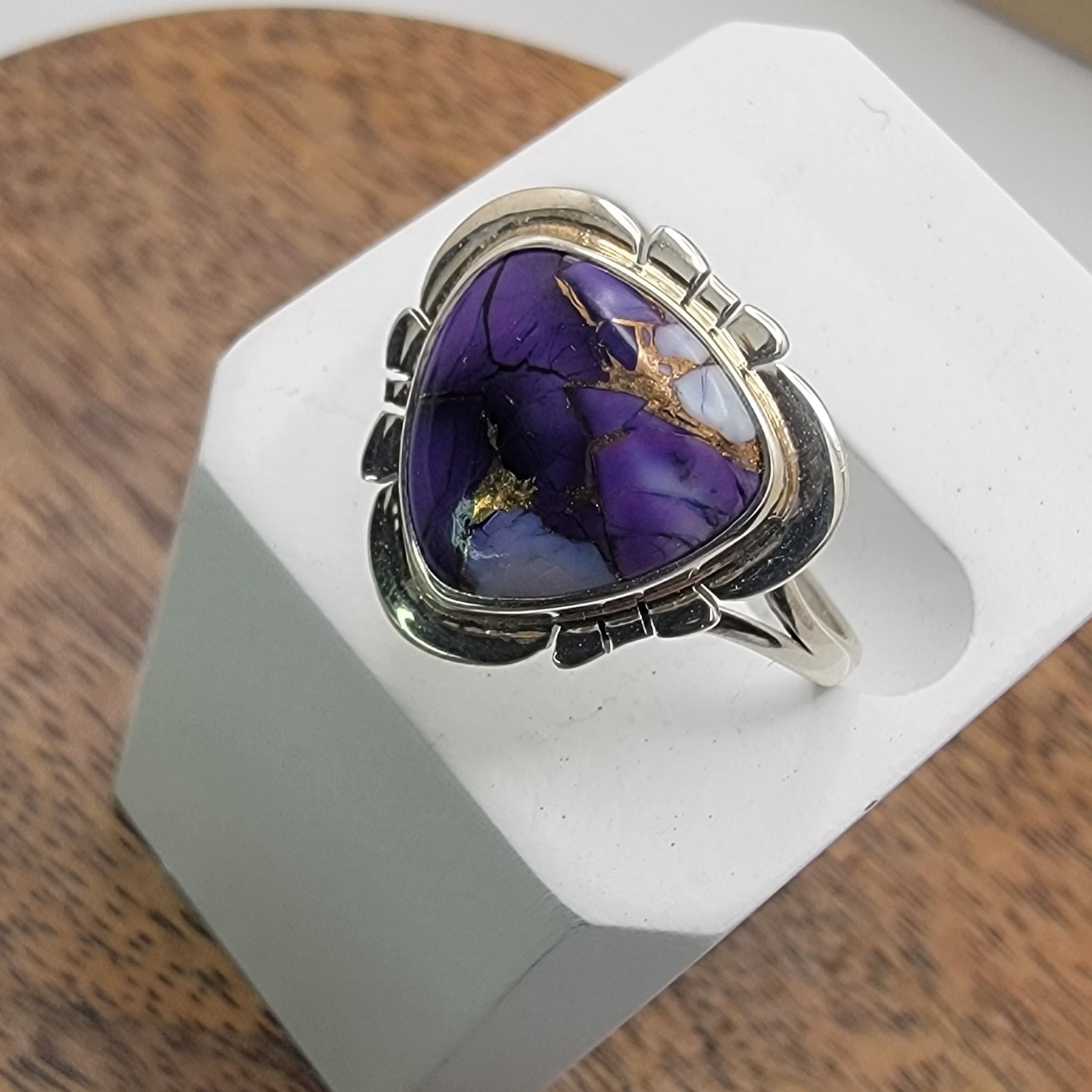 Silver ring with a purple stone on a white stand against a wooden background