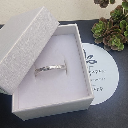 Silver ring in a white box with a plant in the background