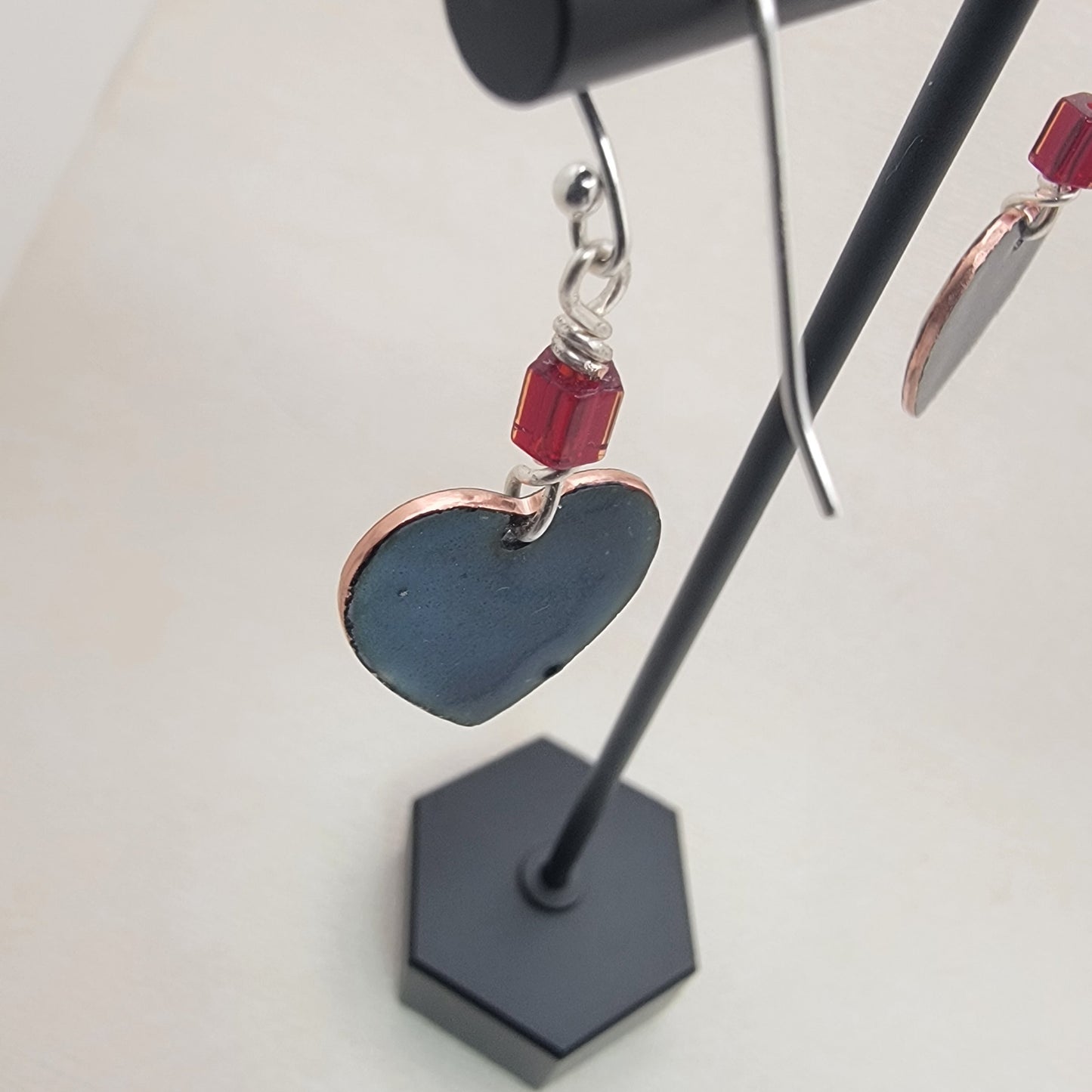 Heart-shaped earrings with red beads on a black stand against a white background