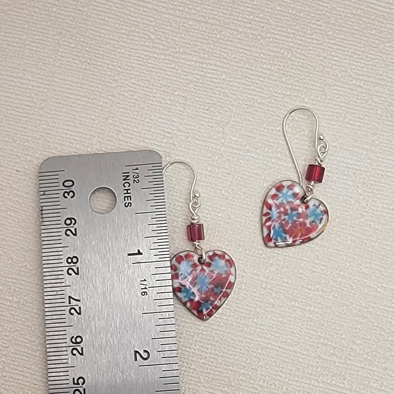 Heart-shaped earrings with floral pattern next to a ruler on a textured surface