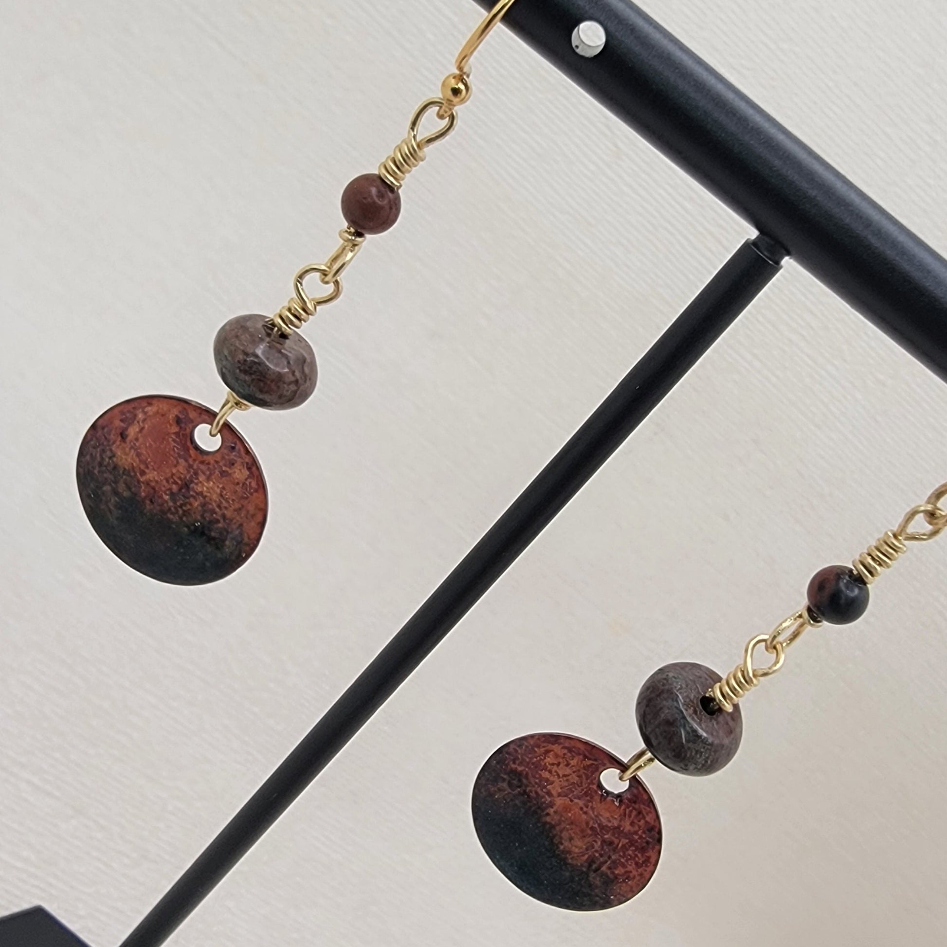 Pair of earrings with brown beads and gold chains on a black stand against a light background
