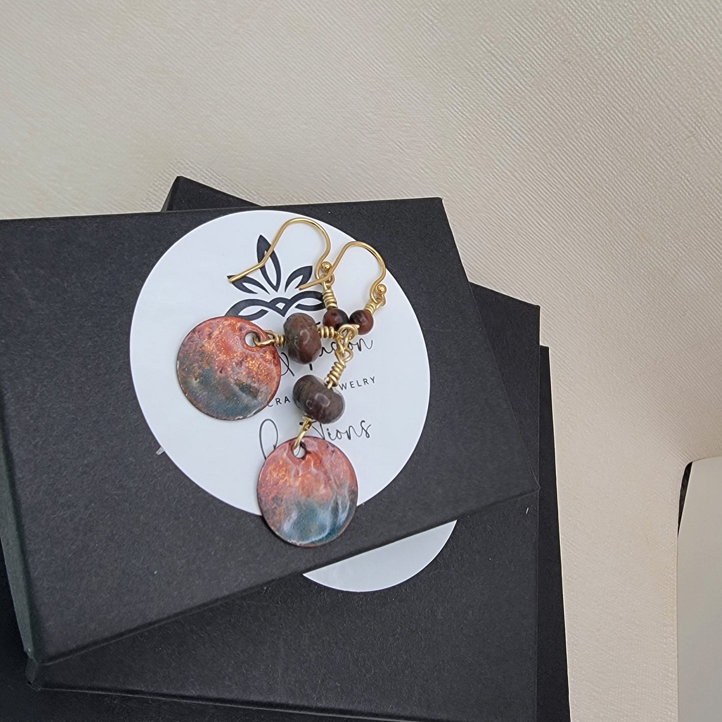 Pair of earrings on a black card with a circular design, placed on a light surface.
