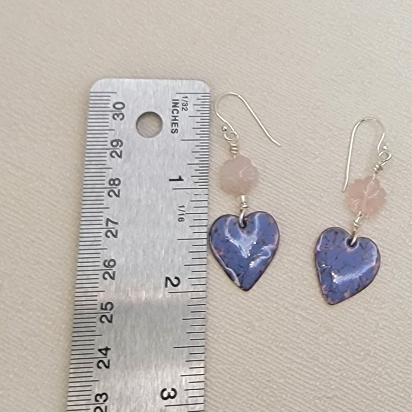 Heart-shaped earrings with pink beads next to a ruler on a beige background