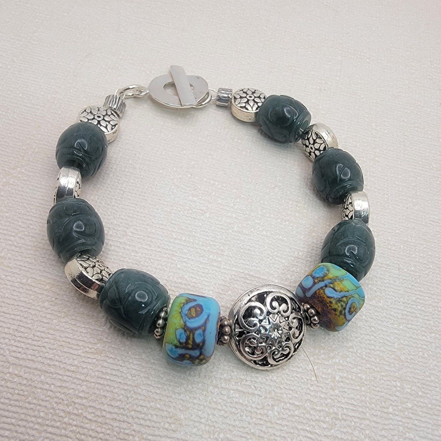 Beaded bracelet with green and sterling silver beads and a silver toggle on a neutral background