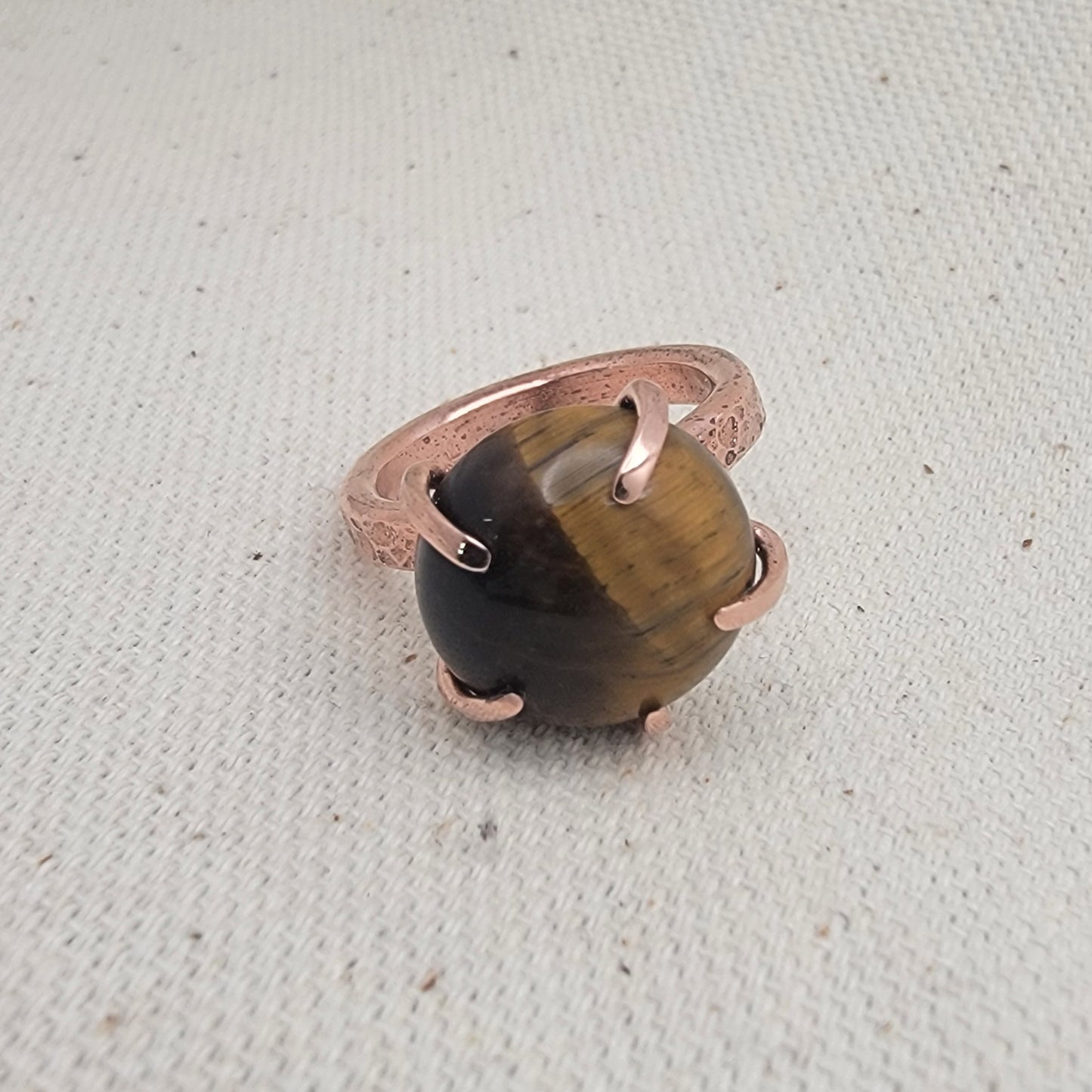Ring with a tiger's eye stone and rose gold band on a textured beige background