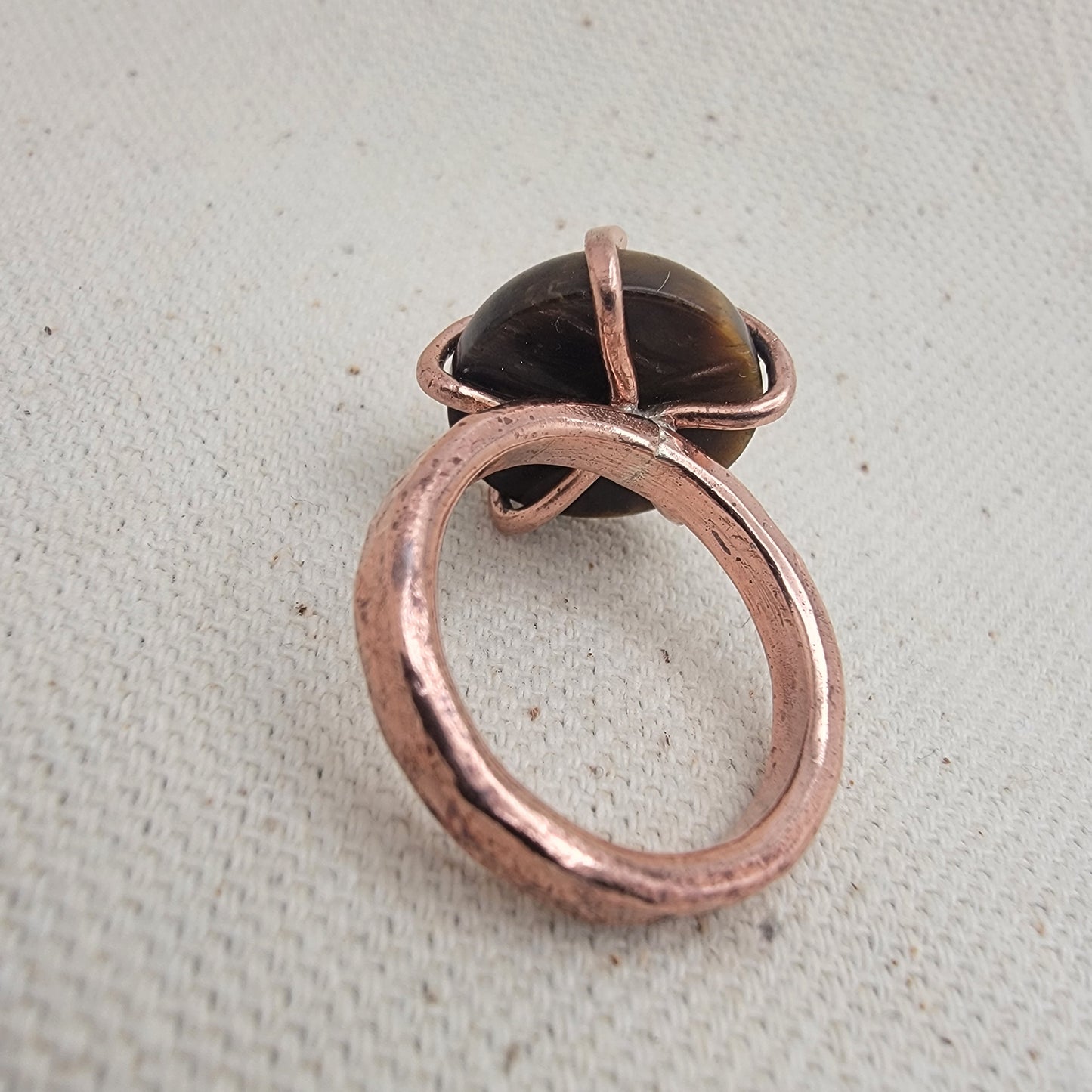 Copper ring with a dark gemstone on a textured beige background