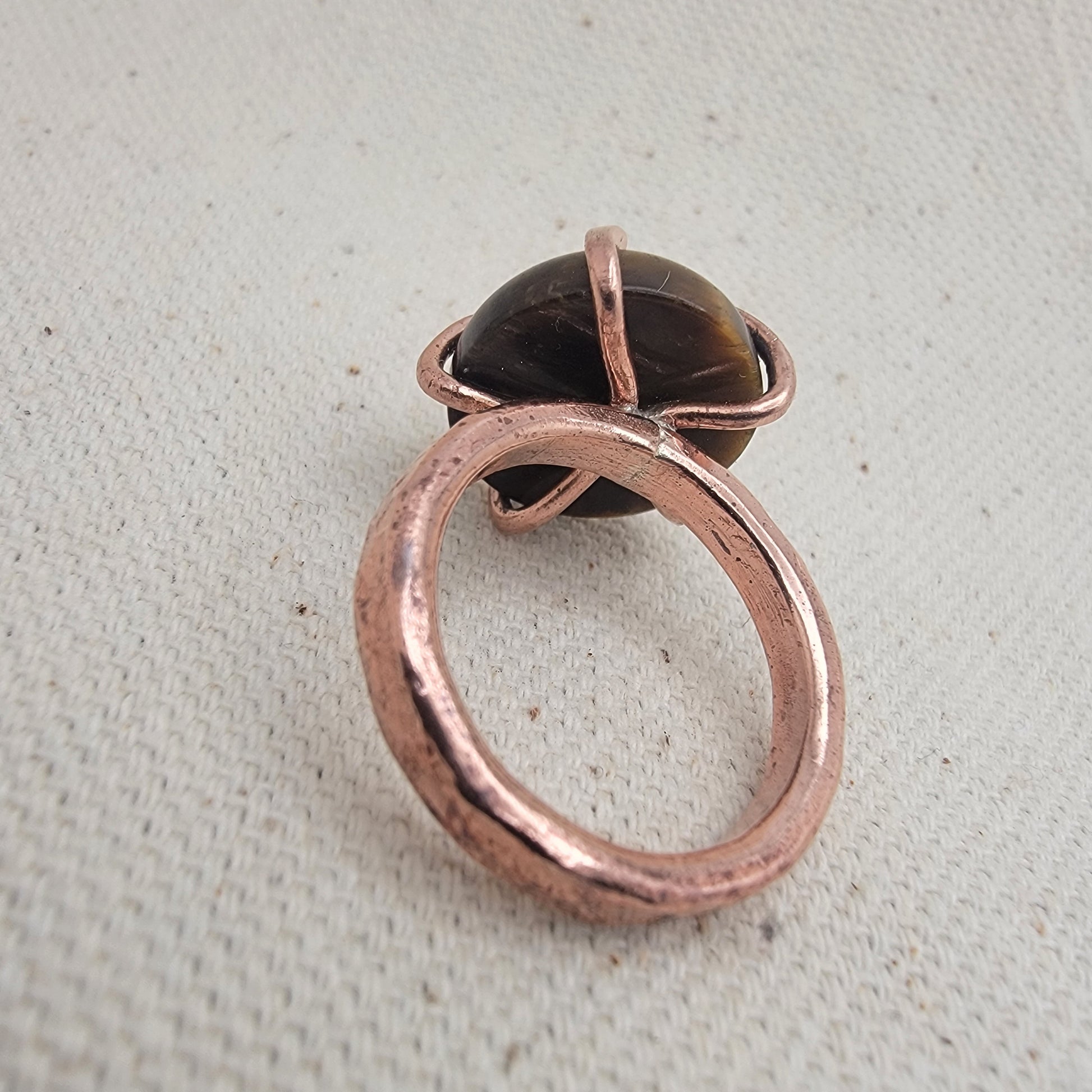 Copper ring with a dark gemstone on a textured beige background