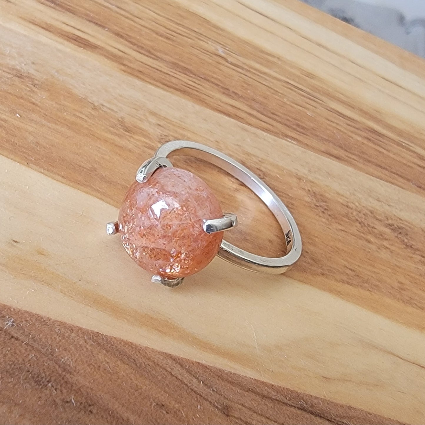 Silver ring with a pink stone on a wooden surface