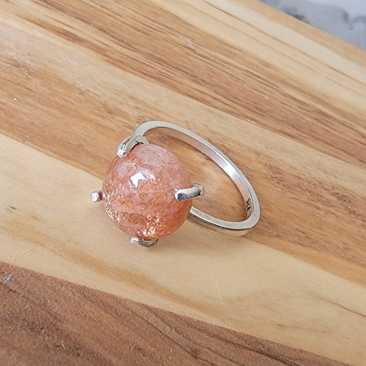 Silver ring with a pink stone on a wooden surface