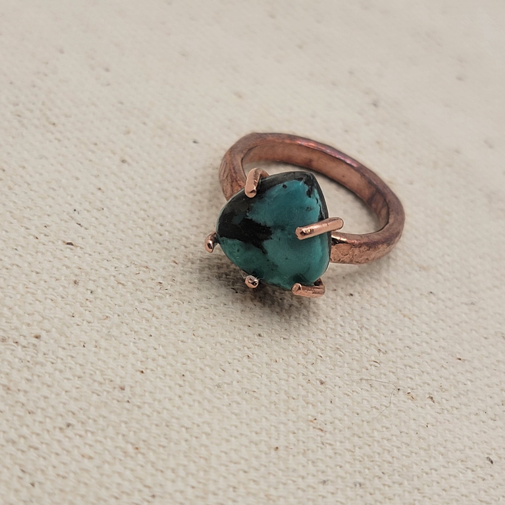 Hammered texture copper and turquoise ring on beige background