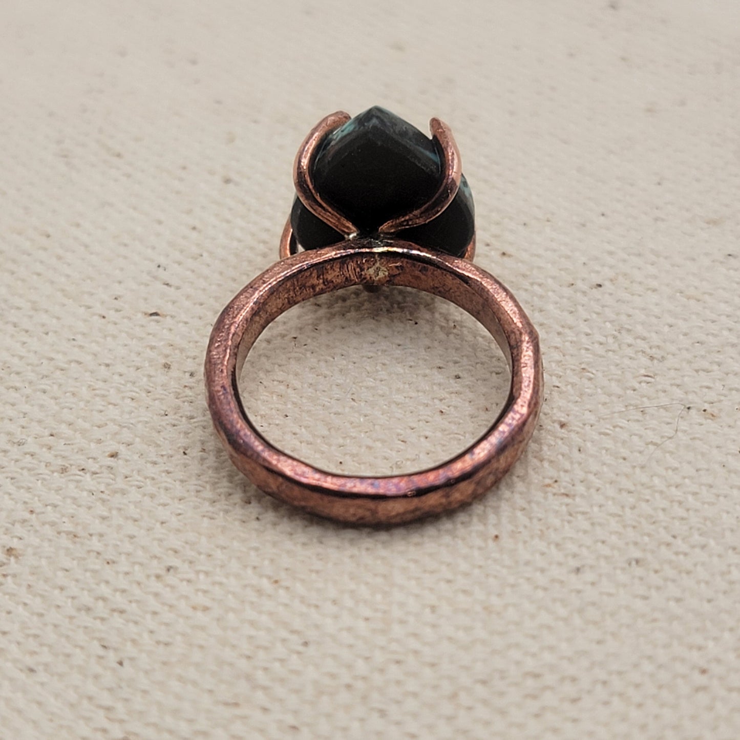 Back view of copper and turquoise ring on beige background.