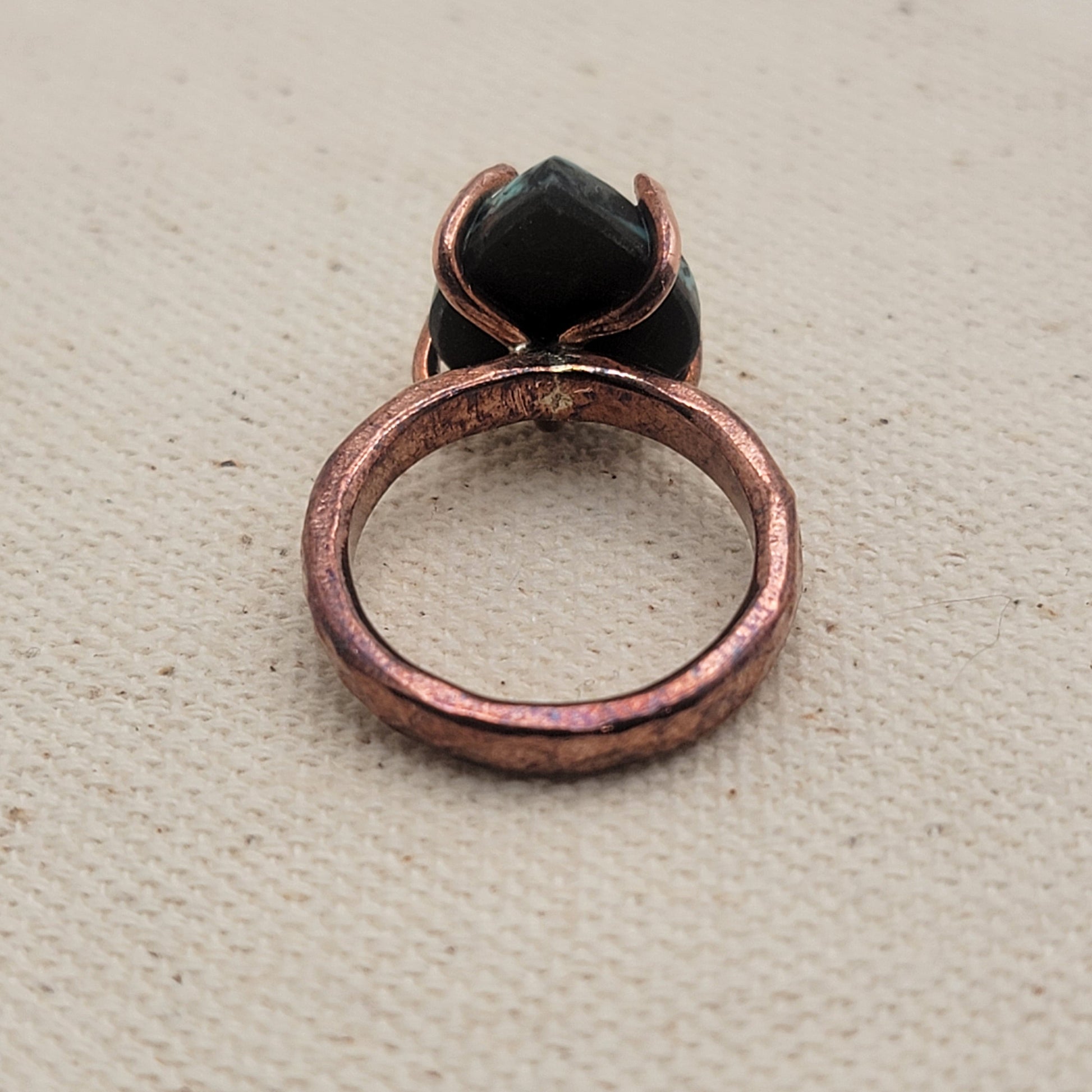Back view of copper and turquoise ring on beige background.