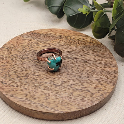 Turquoise and copper ring on wood platform with plant on beige background