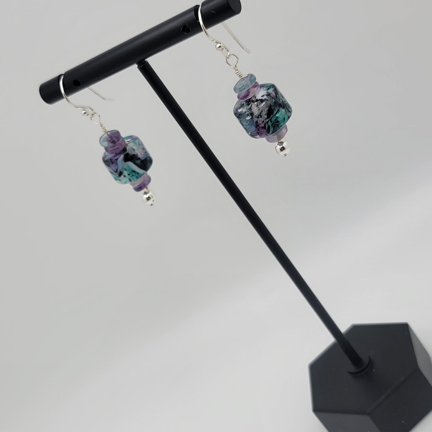 Pair of earrings with colorful beads on a black stand against a white background