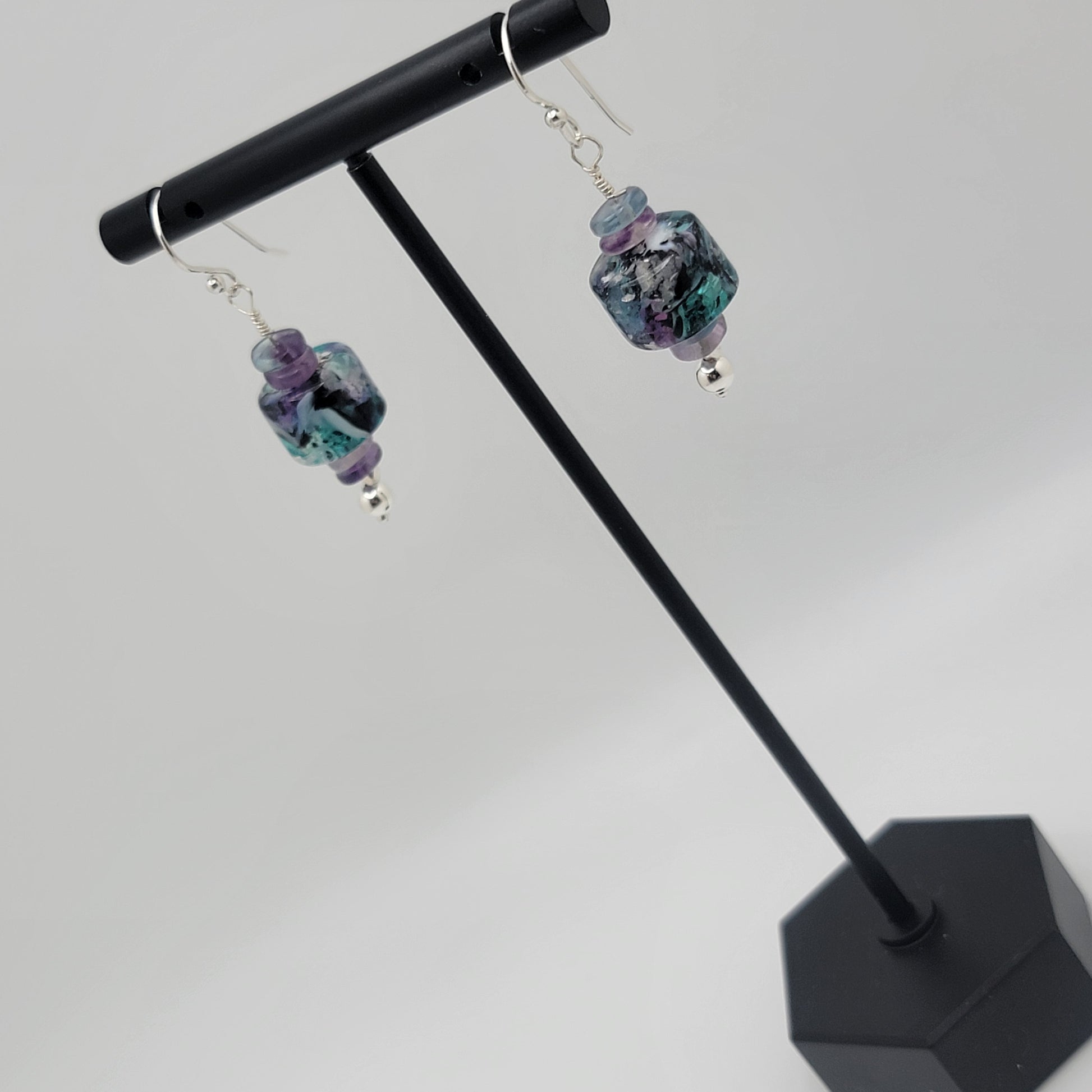 Pair of earrings with colorful beads on a black stand against a white background
