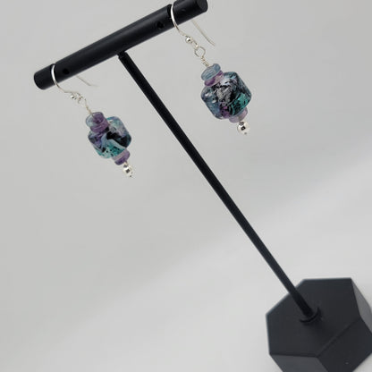 Pair of earrings with colorful beads on a black stand against a white background