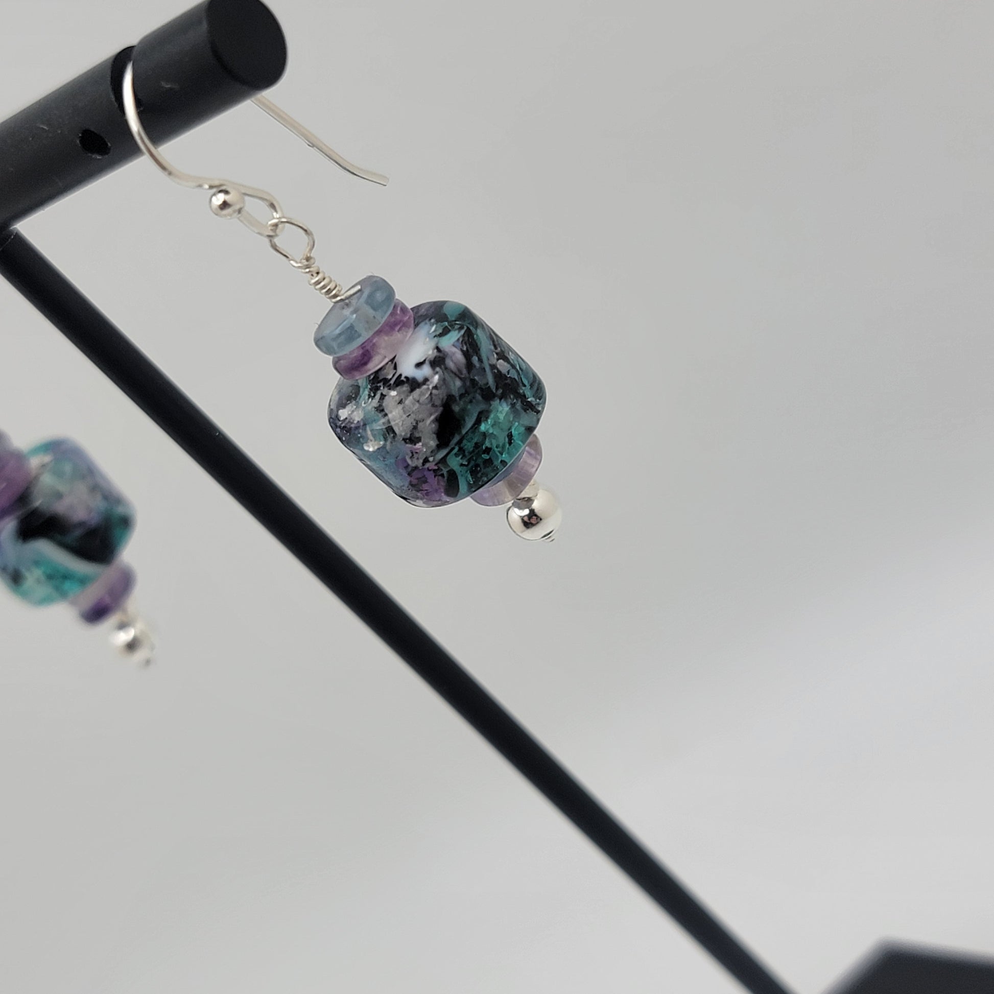 Multicolored beaded earrings on a stand against a gray background